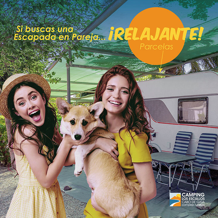 Pareja de mujeres jóvenes sosteniendo un perro, frente a una caravana con el texto "Si buscas una escapada en pareja... ¡relajante!