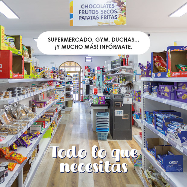 Todo lo que necesitas - Supermercado, gym, duchas, ¡y mucho más! Infórmate Uno de los pasillos del supermercado del camping con estanterías llenas de diferentes productos a los lados y al fondo, la caja