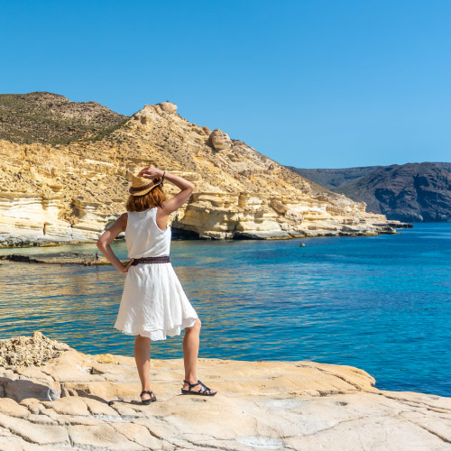 Mujer con un vestido de verano blanco y sombrero de paja, de espaldas mirando al mar